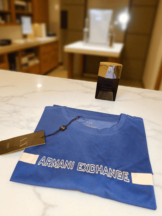 Camiseta Armani azul doblada con etiqueta visible, diseño con logo Armani Exchange. Ropa de alta gama que refleja elegancia y prestigio.